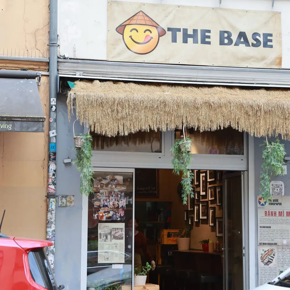 Ladenfront von The Base mit Bastdach, Pflanzen und dem Bánh-Mì-Menü am Eingang